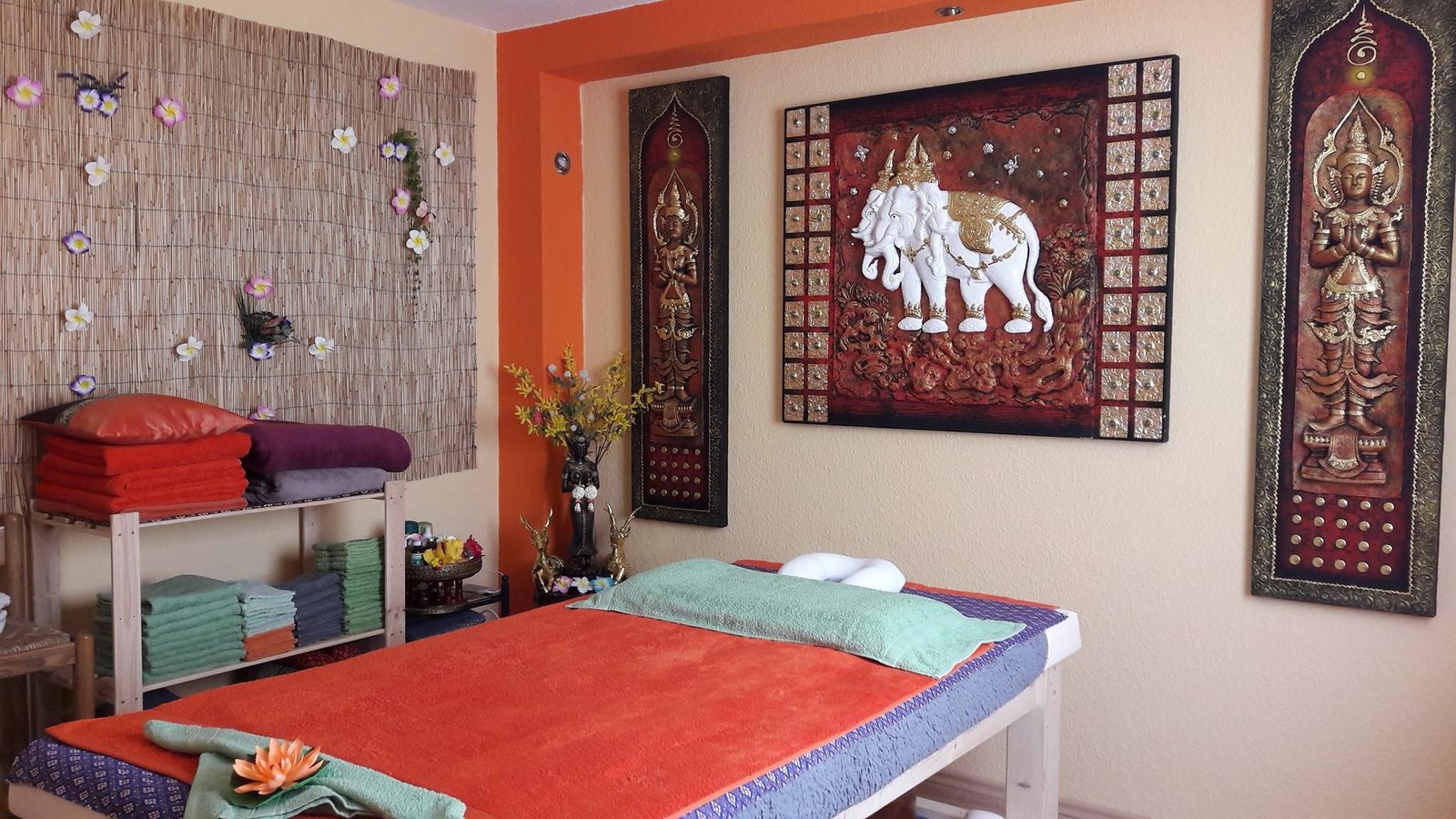 Behandlungsraum mit Thai-Reliefs, Massageliege und Handtüchern